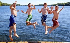 A father and his three boys joyfully leap into the water at Gloucester Pool in Muskoka, Ontario.