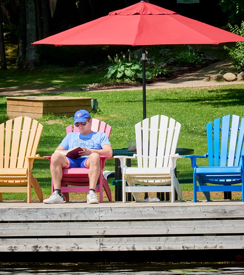 Man reading a book on a Muskoka chair at the dock